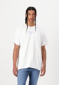 Hvid bomulds T-shirt med afslappet pasform, korte ærmer og blå trykte logo detaljer på brystet; parret med lysblå denim jeans.