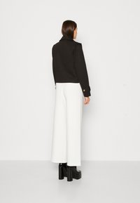 Skórzana kurtka w czerni z kołnierzykiem, złotymi guzikami na rękawach, zestawiona z szerokimi białymi spodniami i czarnymi butami na platformie.