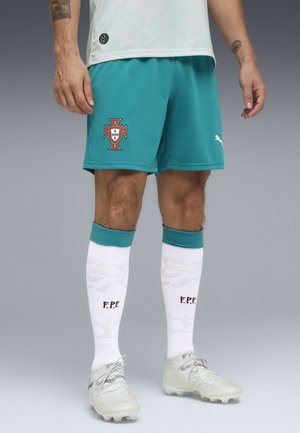 Männliche Beine in türkisfarbenen Fußballshorts von Portugal, weiße Socken mit den Initialen "F.P.F." und hellfarbene Fußballschuhe vor grauem Hintergrund.
