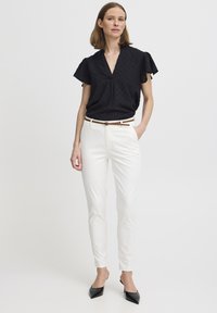 Top nero a maniche corte con scollatura a V e motivo testurizzato, abbinato a pantaloni bianchi sartoriali e una cintura marrone. Tacchi a punta neri.