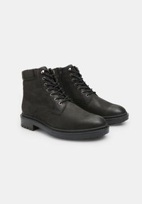 Botas negras de cuero hasta el tobillo con superficie texturizada, cordones en la parte delantera, cierre de cremallera y suelas de goma resistentes. Presentan ojales decorativos de metal.