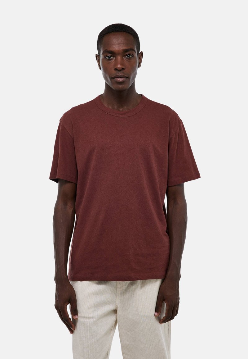 T-shirt en coton bordeaux avec un col rond, des manches courtes et une coupe décontractée. Texture lisse sans motifs ni accents visibles.