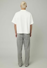 Polo blanc à manches courtes avec une coupe boxy et un col plat, associé à un jean en denim gris taille haute avec des poches arrière.