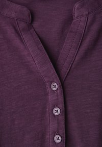 Purpurové tričko Henley s texturovanou tkaninou, částečným zapínáním na čtyři knoflíky a jemným detaily límce.