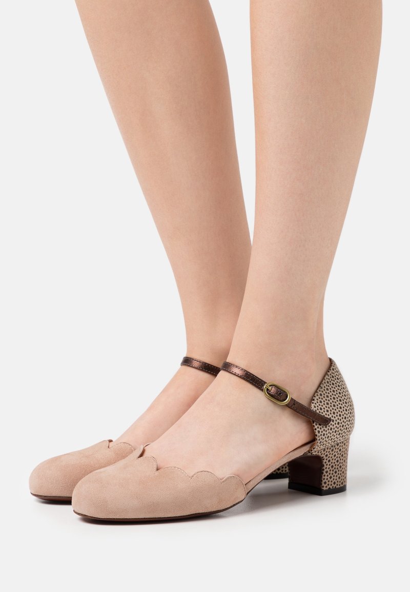 Chaussures en daim beige avec un bord festonné, une bride de cheville marron, et un motif à pois sur le talon. Design à talon carré bas.