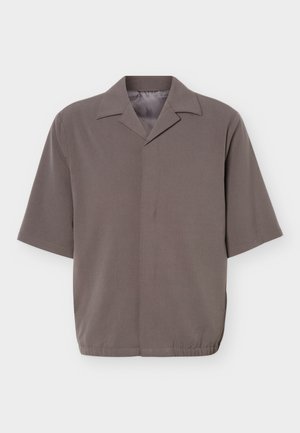 Chemise grise à manches courtes, coupe ample, avec col pointu et fermeture frontale dissimulée, dotée d'un ourlet élastique à la taille.