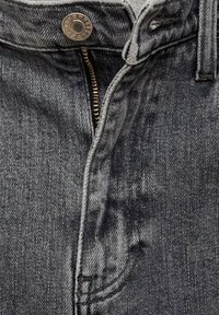 Gros plan d'un jean en denim noir délavé non zippé avec un bouton métallique visible et des dents de fermeture éclair en laiton exposées.