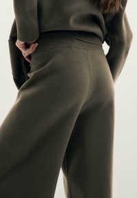 Pantalon en maille douce vert olive avec une taille haute ; design à jambes larges ; texture côtelée à la taille ; détails discrets de coutures.