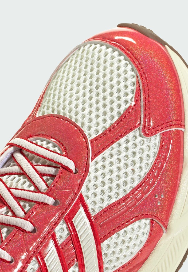 Sneaker rosso e bianco con tomaia in rete, dettagli lucidi e sovrapposizioni testurizzate. Include lacci rosa e suola in gomma.