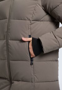 Puffjacka i dämpad brun med quiltad struktur, sidofickor med dragkedja och svarta innerfållar. Har slitstarkt material och en elegant design.