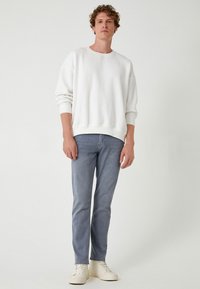 Sudadera blanca de corte relajado, con cuello redondo y mangas ajustadas, combinada con jeans ajustados de un azul claro y zapatillas color hueso.