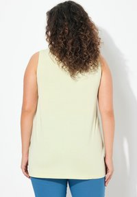 Canotta di colore giallo chiaro con una vestibilità comoda e orlo arrotondato, realizzata in tessuto morbido. Design senza maniche con una trama semplice e senza motivi visibili.