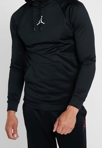 Felpa nera a maniche lunghe con cappuccio, realizzata in tessuto elasticizzato, dotata di tasca a marsupio frontale e logo bianco sul petto. Texture liscia; design aderente.