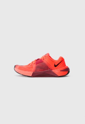 Lys orange og maroon Nike treningssko med mesh-overdel, svart swoosh-logo og teksturert såle vist i sideprofil på hvit bakgrunn.