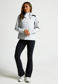 Light gray windbreaker jacket with a high collar, zip closure, and black accents. Paired with black fitted pants and white sneakers.