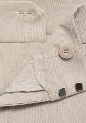 Beige fabric with a smooth texture, featuring a button, zipper, and metal accents, highlighting a well-finished pocket design.