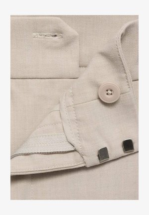 Beige stof med en glat tekstur, der har en knap, lynlås og metaldetaljer, der fremhæver et veludført lomme-design.