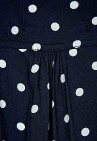 Top in tessuto navy con pois bianchi e dettagli arricciati in vita. Texture liscia con cuciture sottili visibili.