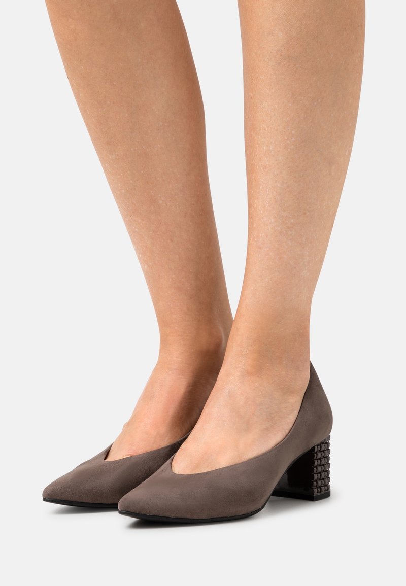 Escarpins en daim gris avec un bout pointu et un petit talon bloc, présentant des accents texturés. Le modèle comporte une découpe en V sur les côtés.