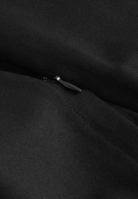 Tela negra con una textura fina que presenta una cremallera pequeña y elegante. El tirador de la cremallera es metálico, complementando el color oscuro en general.