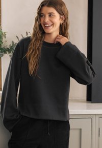 Dunkelgraues Sweatshirt mit lockerem Schnitt, breiten Bündchen und rundem Ausschnitt. Weicher Stoff und glatte Textur, kombiniert mit einem gerippten Saum.