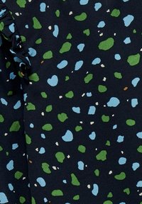 Tissu foncé avec un fond texturé bleu marine, présentant des taches irrégulières en bleu, vert et crème, avec un bord légèrement ondulé.