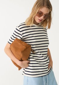 Stribet hvid og marineblå t-shirt, afslappet pasform, parret med en blød brun ruskinds clutch; model med store brune solbriller.