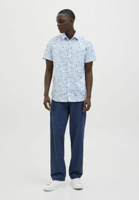 Kurzarmhemd in hellblau mit floralem Muster, kombiniert mit locker sitzenden marineblauen Hosen und weißen Sneakers.