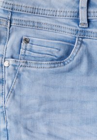Ljust blått denimtyg som visar en närbild av ett framfickans område med en sydd kant och en metallknapp som accent.