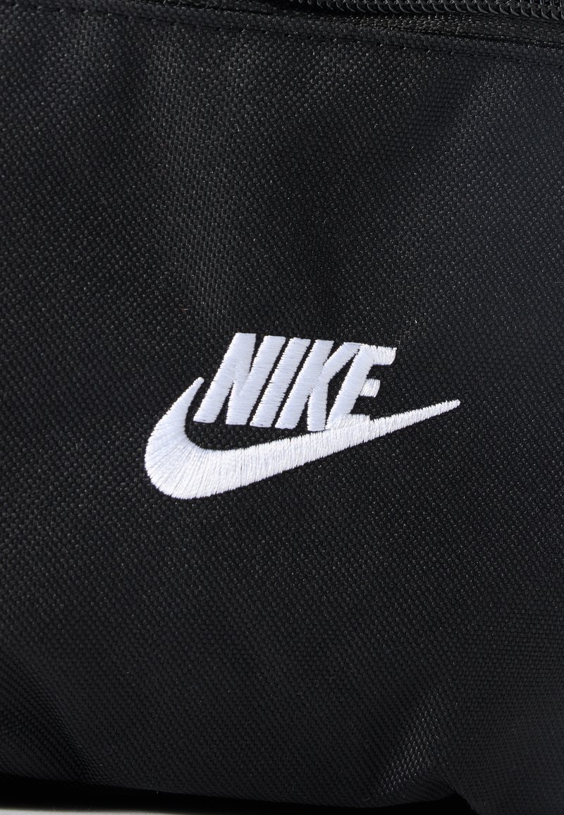 Black fabric surface with a white Nike logo embroidery, including the brand name and swoosh symbol.