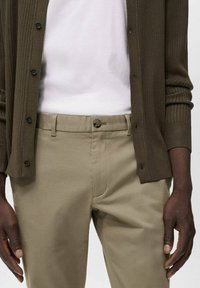 Brun ribbad cardigan över en vit t-shirt, i kombination med ljusbeige byxor. Anmärkningsvärda detaljer inkluderar knapplåsningar och mjuka texturer.