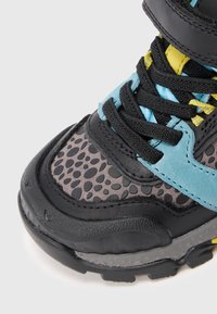 Børnesneakers med sorte snørebånd, sort og grå plettet tå, lys blå detaljer, gule detaljer og en tyk sort sål.