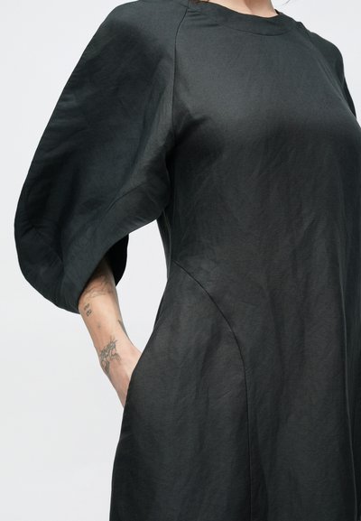 Μαύρο φόρεμα από υφασμάτινη υφή, με στρογγυλή λαιμόκοψη, φουσκωτά μανίκια και πλαϊνές τσέπες, στενή μέση.