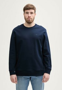Marineblaues Sweatshirt mit langen Ärmeln, rundem Halsausschnitt und gerippten Bündchen. Verfügt über ein kleines Logo auf der Brust. Aus glattem Baumwollmischgewebe.