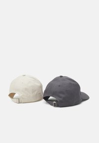 Due cappellini da baseball sono esposti da dietro. Uno è di un beige chiaro, e l'altro è grigio scuro. Entrambi hanno una texture di tessuto e una fibbia regolabile.