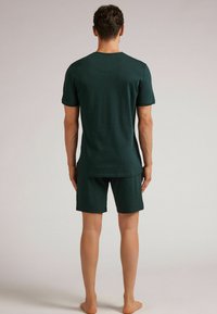Dunkelgrünes T-Shirt mit kurzen Ärmeln und rundem Halsausschnitt, kombiniert mit passenden Shorts. Beide aus glattem Stoff und mit lässiger Passform.