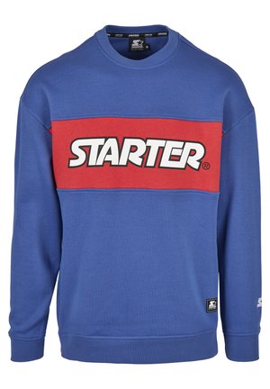 Zila sporta džemperis ar sarkanu horizontālu svītru, uz kuras rakstīts "STARTER" baltā krāsā. Arapa kakls, garas piedurknes, ribinātās piedurknes un apakšmalas.