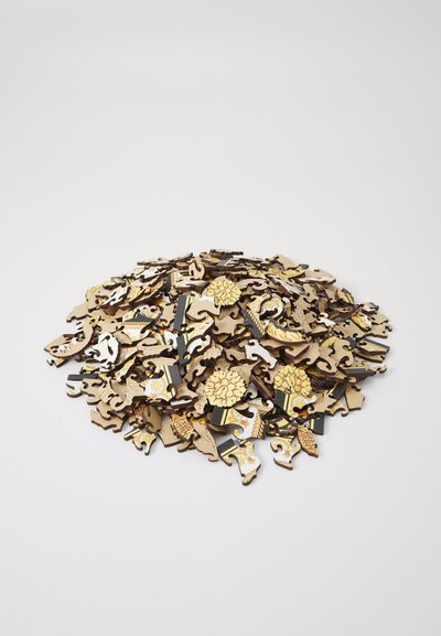 Wooden jigsaw puzzle pieces in varying shapes, featuring intricate designs in gold, black, and white, stacked haphazardly on a white surface.