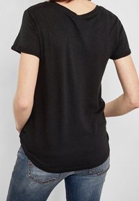 Czarny t-shirt z krótkim rękawem i okrągłym dekoltem; miękka tekstura i luźny krój, w połączeniu z niebieskimi dżinsami.