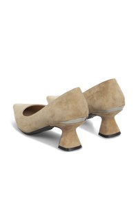 Scarpe con tacco alto in suede beige con schienale arrotondato e tacco a flusso. Presentano una suola nera piatta e dettagli metallici sul tacco.