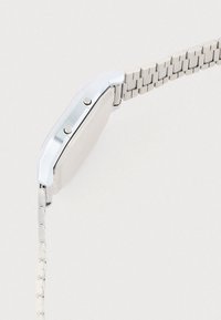 Ασημένιο μεταλλικό ρολόι χειρός με ορθογώνια κάσα, λεία επιφάνεια και λουράκι με συνδέσμους. Διαθέτει δύο κουμπιά στο πλάι για ρυθμίσεις.