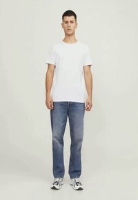 Camiseta branca de algodão, com decote redondo, corte descontraído, combinada com jeans azul desgastado, de perna reta, e ténis pretos e brancos.