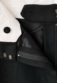 Intérieur d'une veste en tissu noir avec un col crème, une fermeture éclair en argent et des boutons. Possède une doublure lisse et des textures contrastées.