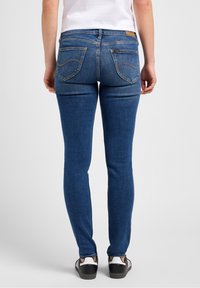 Smal blå jeans i denim, med två bakfickor med krökta sömmar och en läderlapp på midjebandet. Bärs med svarta sneakers.