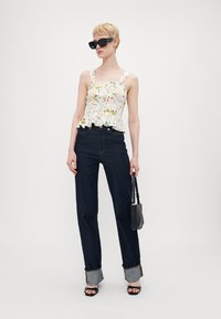 Blomsterpeplumtop med tykke stropper, parret med høyt liv mørke denimjeans med brettede mansjetter; modellen holder en liten svart veske og har solbriller på.