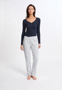 Mörkblå långärmad henley-tröja med knappar, ihop med vita mönstrade pyjamasbyxor med blå blommönster, tillverkade av mjukt tyg.