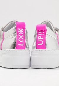 Srebrne sneakersy z białymi podeszwami mają jasnoróżowe pętle przy pięcie z wyświetlonymi słowami "LOOK" i "UP!!!" białymi literami.