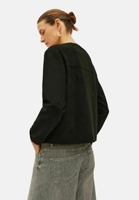 Svart mockajacka med långa ärmar, kortad design, detaljerad ryggparti, tillsammans med ljusgrå högmidjade jeans. Slät textur.