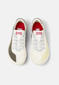 Vita och grå sneakers med en texturerad tyg, med gröna och gula accenter, snörning och en framträdande röd logotyp på tungan.
