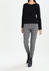 Černý přiléhavý top s dlouhým rukávem, zkombinovaný se slim fit šedými kostkovanými kalhotami a černými vysokými podpatky. Hladká tkanina a precizní střih.